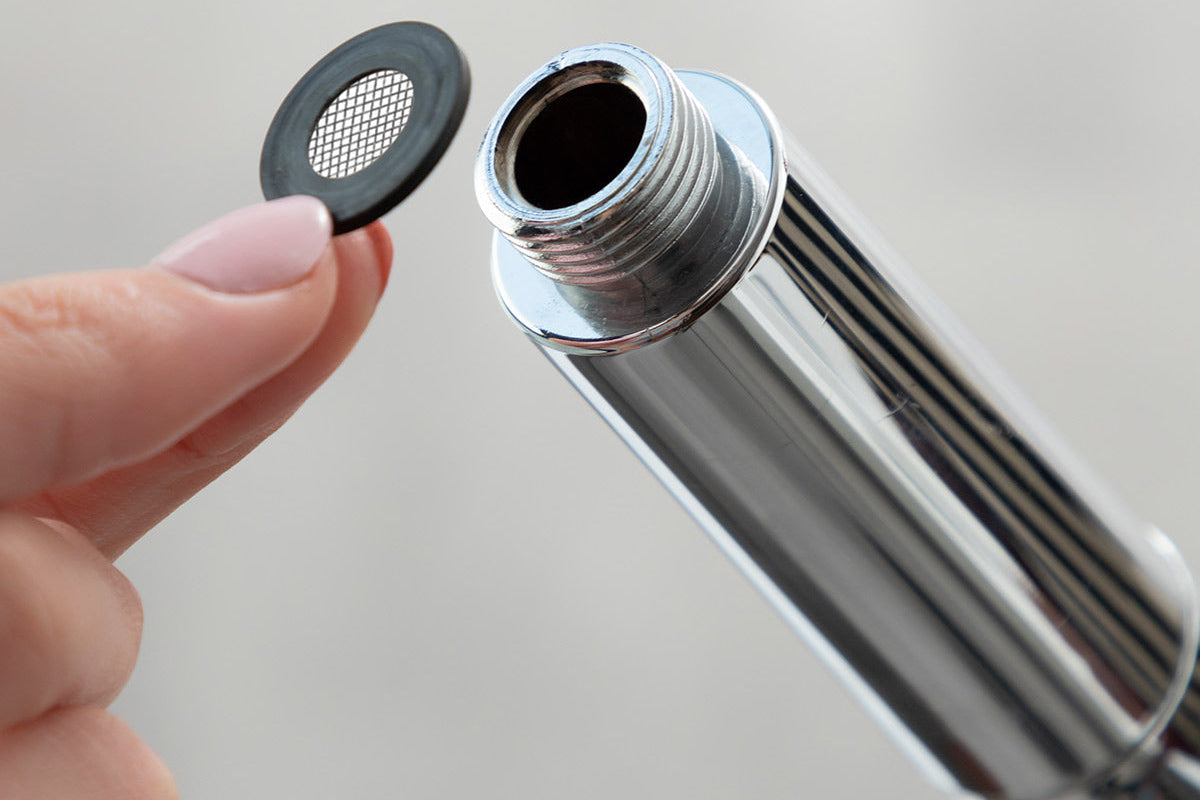 Hand holding a metallic kitchen faucet filter with 'HydraCure' branding on a light gray background.